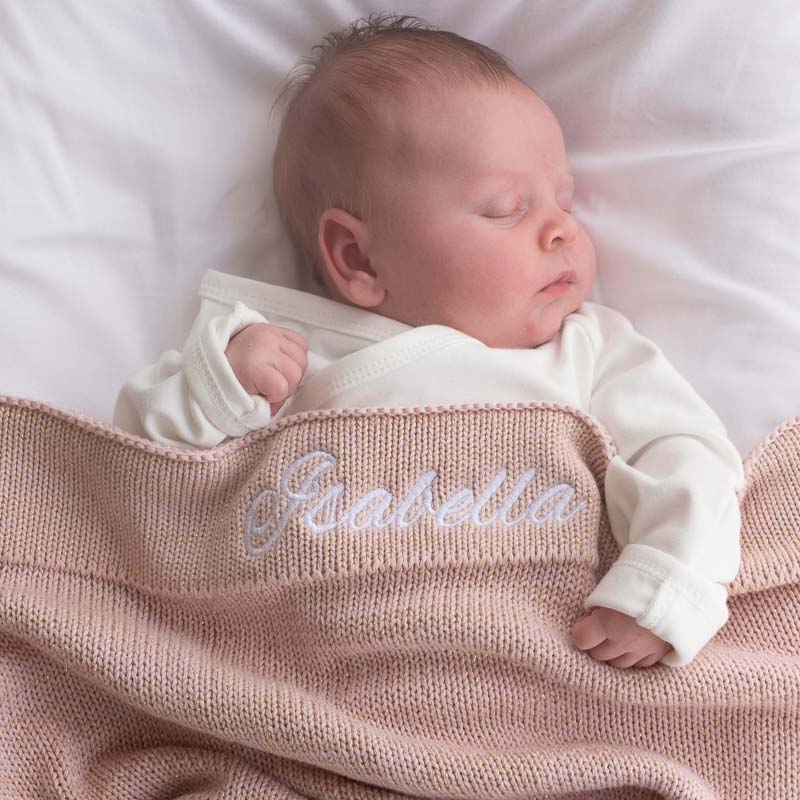 Newborn baby sleeping under a personalised pink knitted blanket.