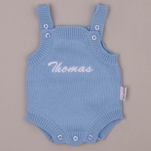 Blue knitted baby romper embroidered “Thomas” in white script.