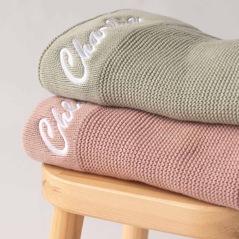 Blush pink and sage green personalised knitted baby blankets stacked.