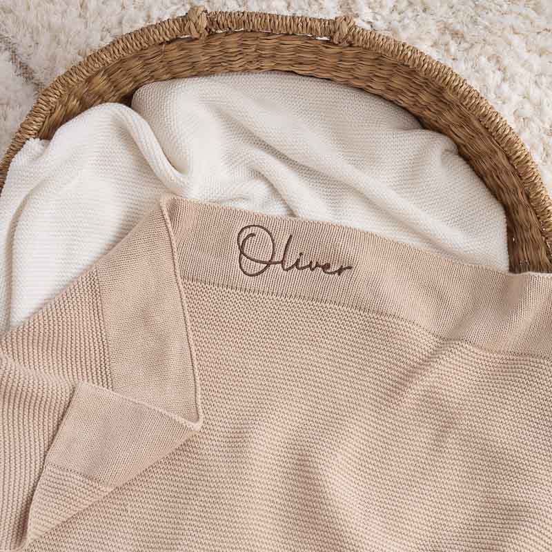 A Personalised Beige Knitted Baby Blanket Embrodiered With Autography Font.