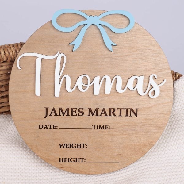 3d Boy Birth Announcement Disc Blue Bow Round wood birth announcement disc with raised white acrylic name, blue acrylic bow and engraved full name and birth detail fields on wicker basket.