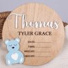 Round wood birth announcement disc with raised white acrylic name, blue acrylic bear and engraved full name and birth detail fields on wicker basket.
