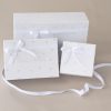3 Baby Gift Boxes With Ribbon Three One Little Day gift boxes in varying sizes tied with white satin ribbon bows on a beige background.