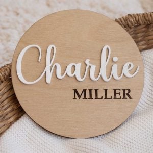 Wooden birth announcement disc with Charlie Miller in raised white lettering.