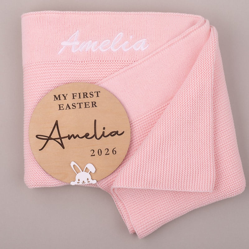 Pink knitted baby blanket with personalised Easter disc showing name Amelia and year 2026.