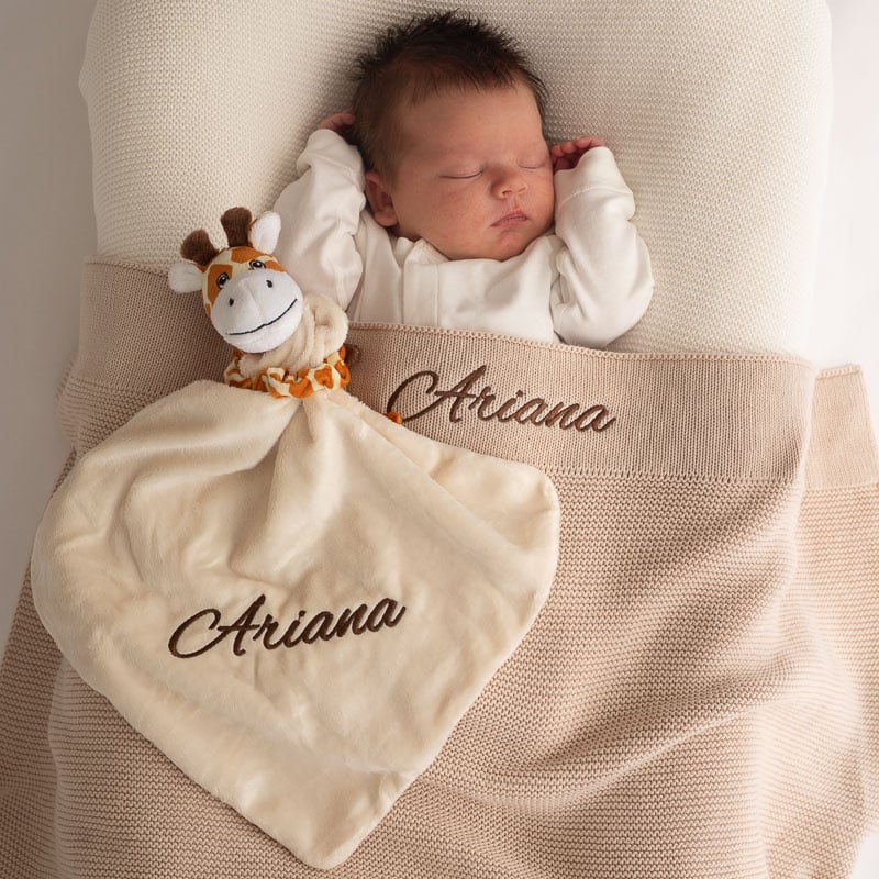 Sleeping baby with personalised beige blanket and giraffe comforter.