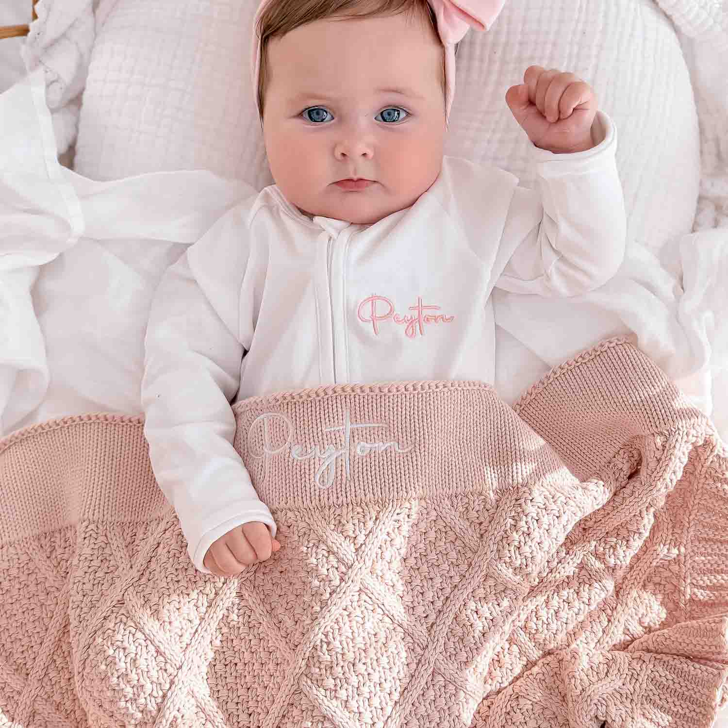 Baby with personalised pink knitted blanket and white zip onesie.
