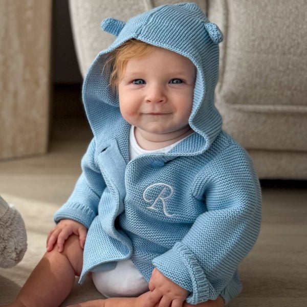 Baby Sitting In A Blue Hooded Knitted Baby Cardigan Initial Baby Sitting In A Blue Hooded Knitted Baby Cardigan with Initial embroidered on front.