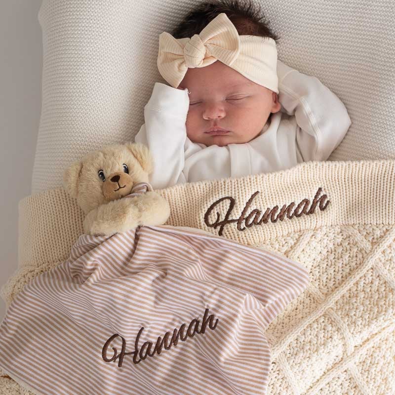 Sleeping baby with cream knitted blanket and personalised bear comforter.