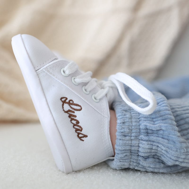 Personalised white baby shoe with embroidered name on baby's foot.