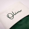 Close-up of personalised pine green velvet baby Christmas stocking with dark green Oliver embroidery on white cuff