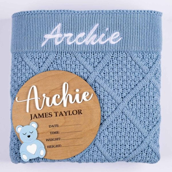 Blue Diamond Knit And Bear Boy Birth Announcment Disc. Archie Blue diamond knitted personalised baby blanket with white embroidered script name displayed alongside a wooden bear birth announcement disc with blue acrylic bear and birth detail fields.