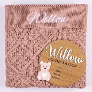 Blush pink diamond knitted personalised baby blanket with white embroidered script name displayed alongside a wooden bear birth announcement disc with pink acrylic bear and birth detail fields.