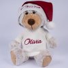 Christmas Bear & Jumper Wearing Santa Hat. Olivia Personalised Christmas Bear teddy in cream jumper embroidered with "Olivia" in burgundy, wearing a white and red Santa hat embroidered "Olivia" in burgundy on the brim, seated against a grey studio background.
