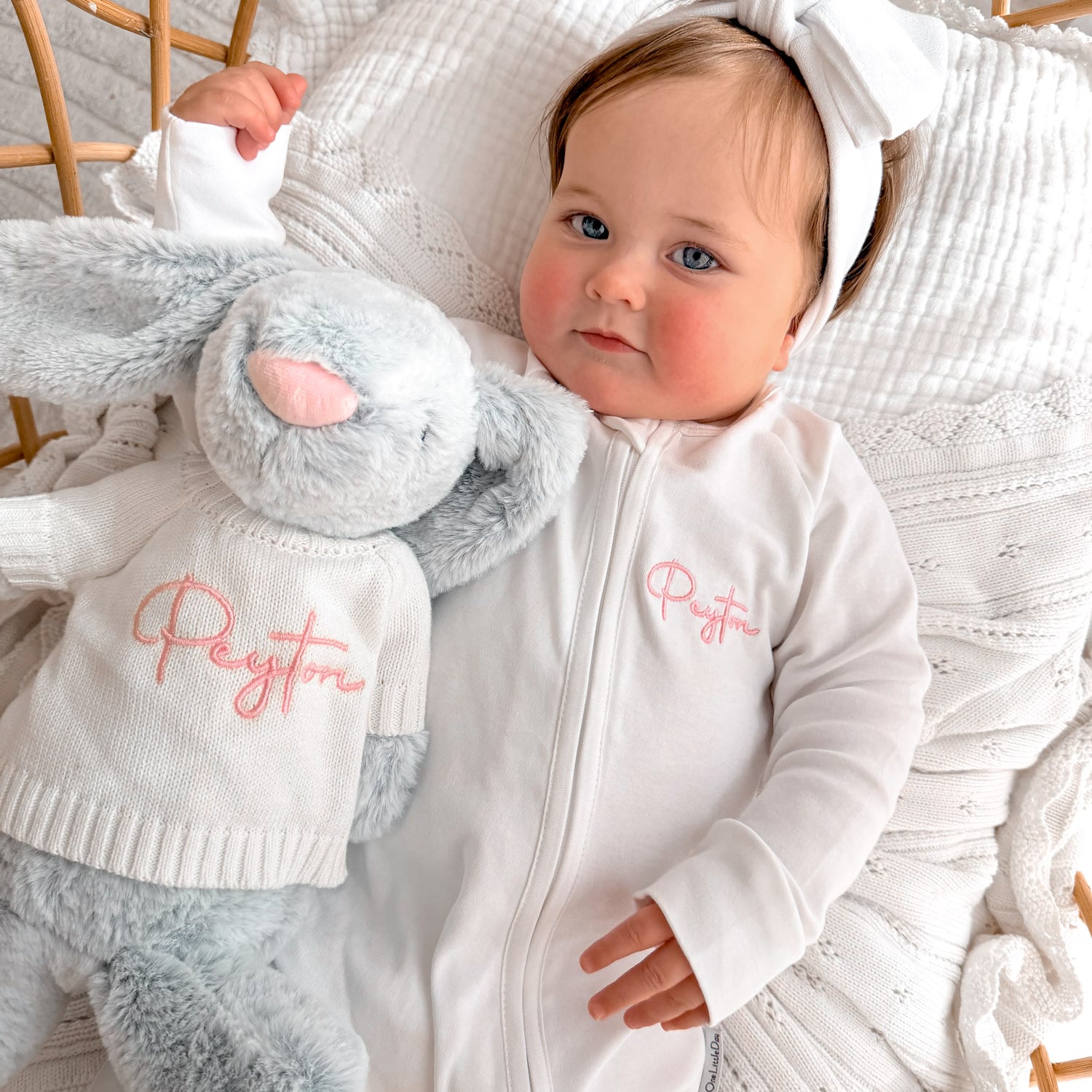 Personalised white zip onesie with Peyton embroidered in pink on baby beside grey bunny plush wearing matching Peyton jumper